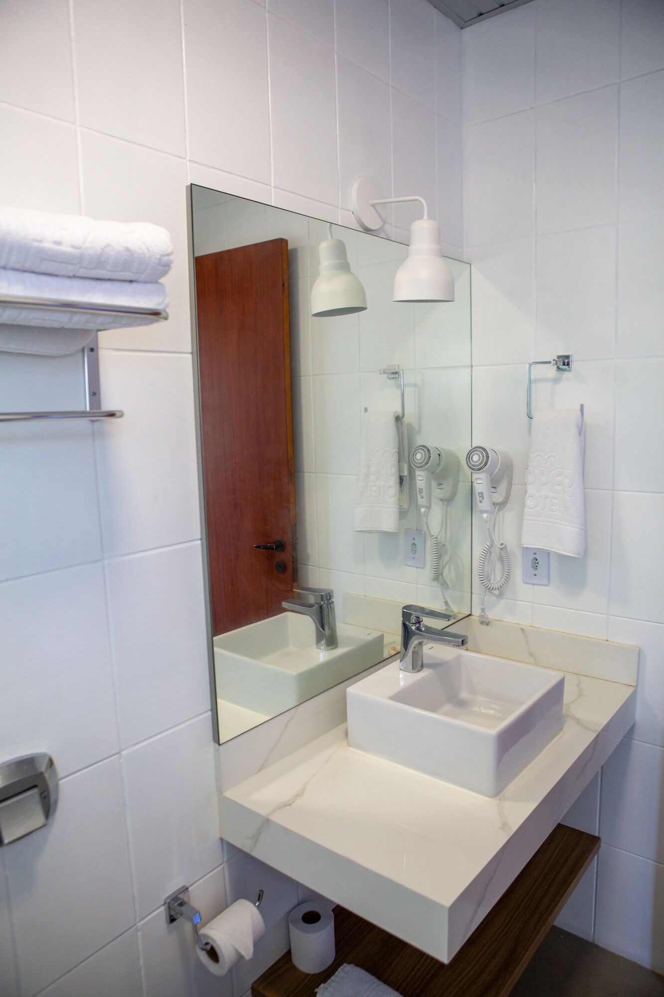 Un baño moderno con un espejo grande, dos lavamanos, un secador de pelo y un perchero para toallas.