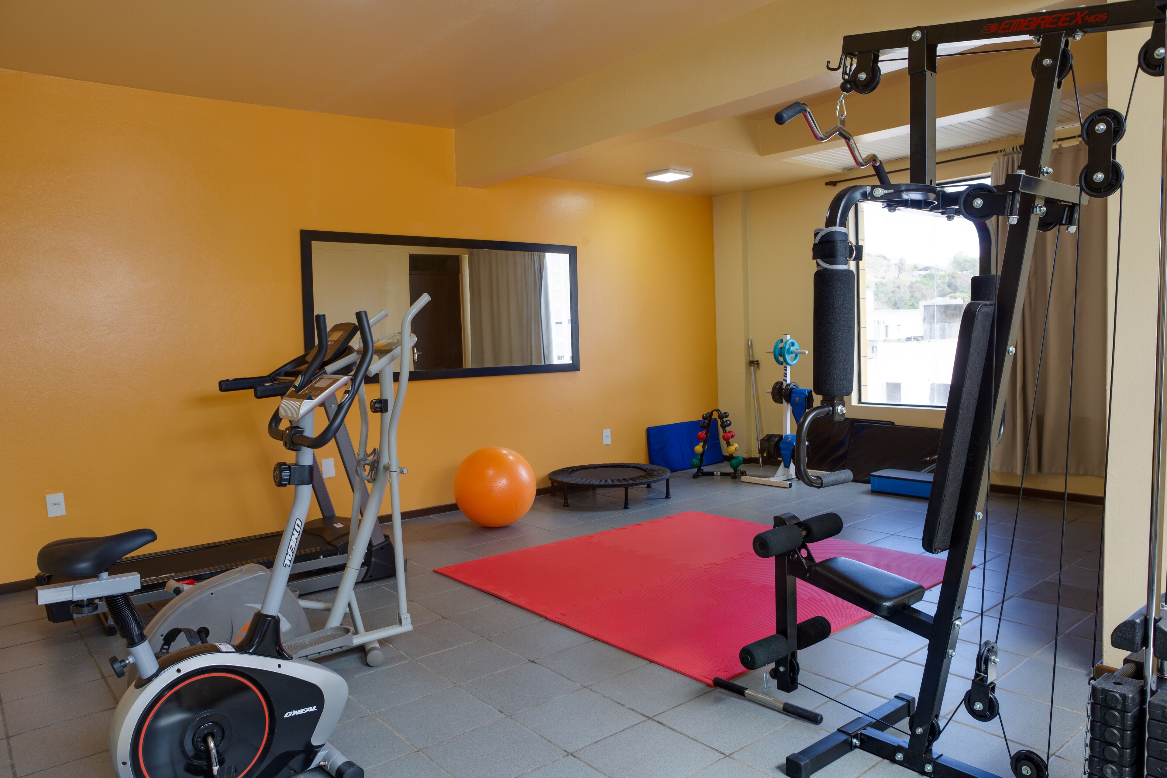 Une salle de sport équipée de matériel d’exercice, avec un tapis rouge et un grand ballon orange.