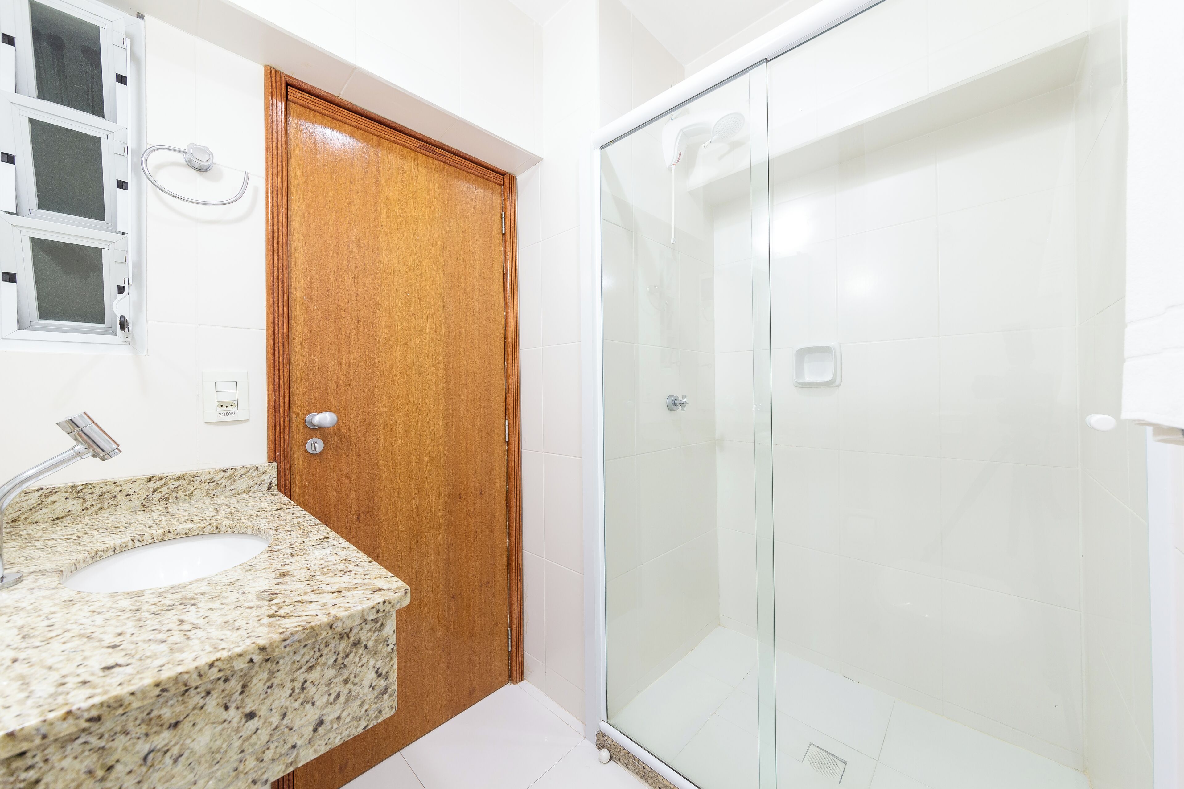 A bathroom with a wooden door, a granite countertop sink, and a glass shower enclosure.