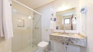 A bathroom with a glass shower enclosure, a white toilet, a granite countertop sink, and a hairdryer mounted on the wall.