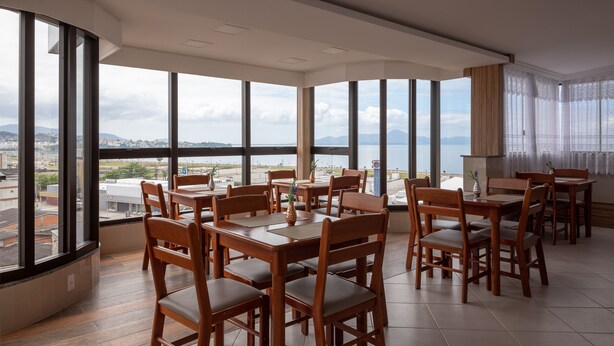 A dining area with wooden tables and chairs, large windows with a view of the city and mountains. - SLIM São José Zion (Sao Jose)