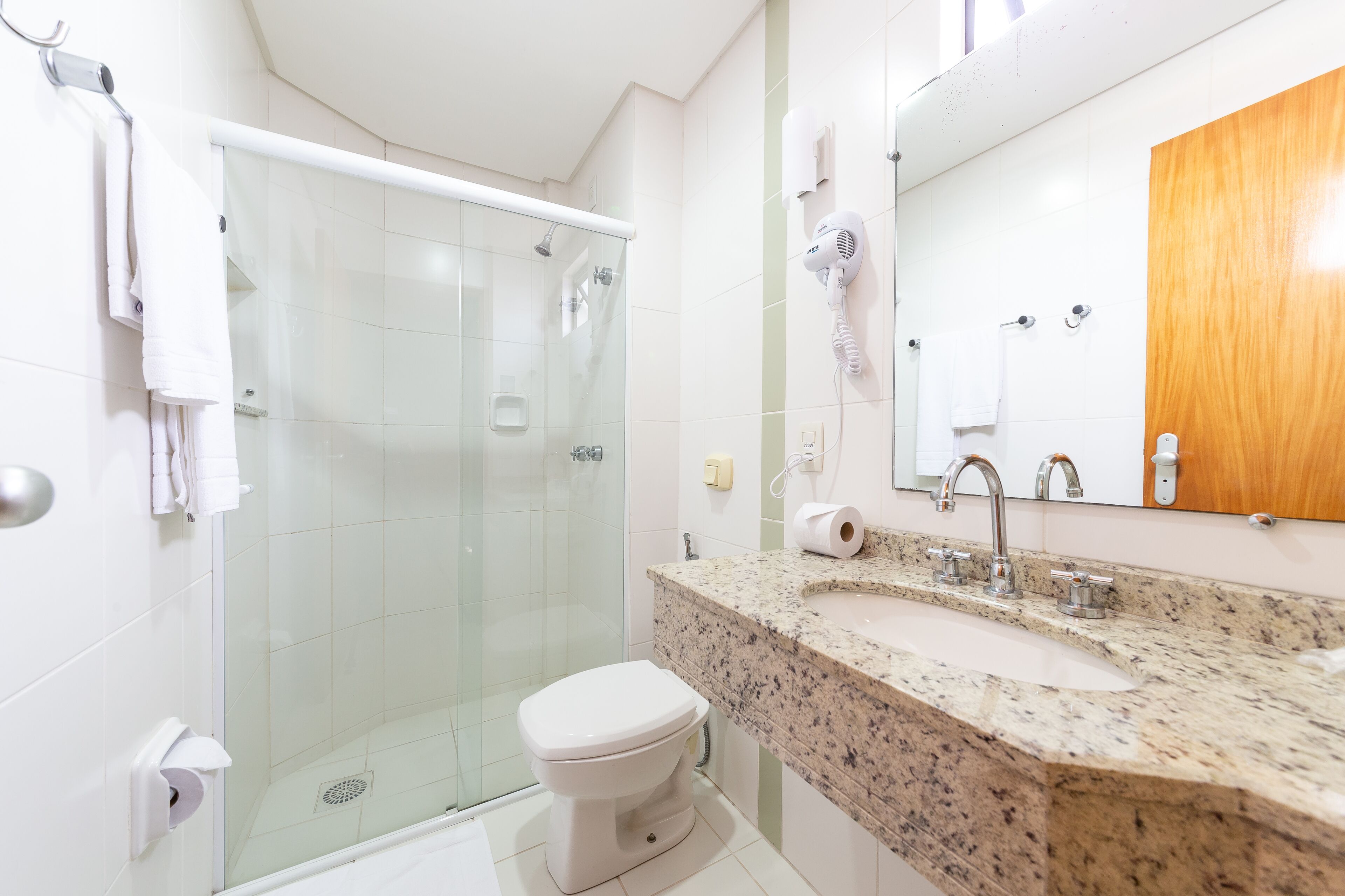 Un baño moderno con ducha de vidrio, inodoro blanco, lavamanos de granito y mueble de madera.