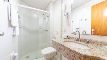Un baño moderno con ducha de vidrio, inodoro blanco, lavamanos de granito y mueble de madera.