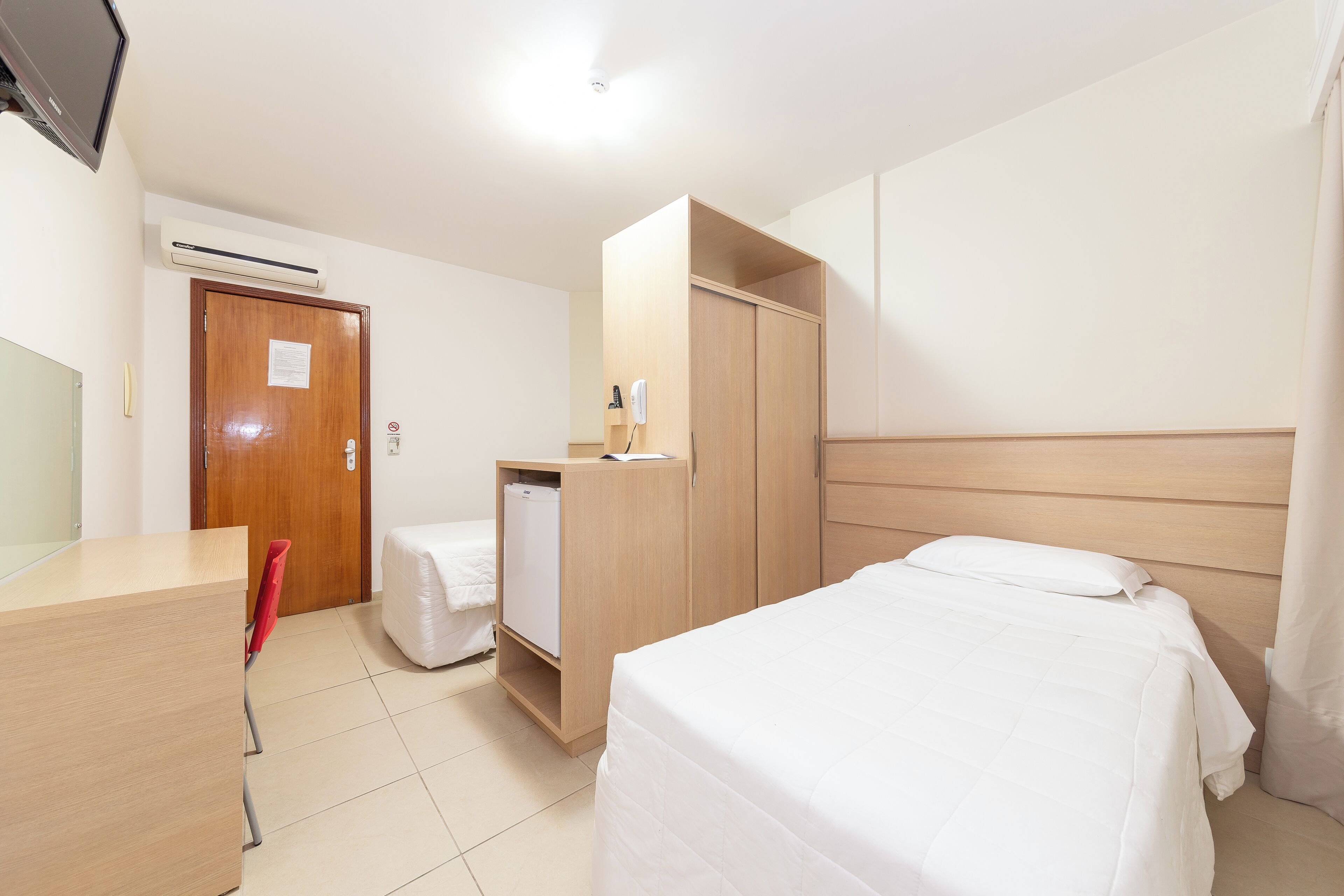 Una habitación de hotel con cama, escritorio, armario y aire acondicionado.