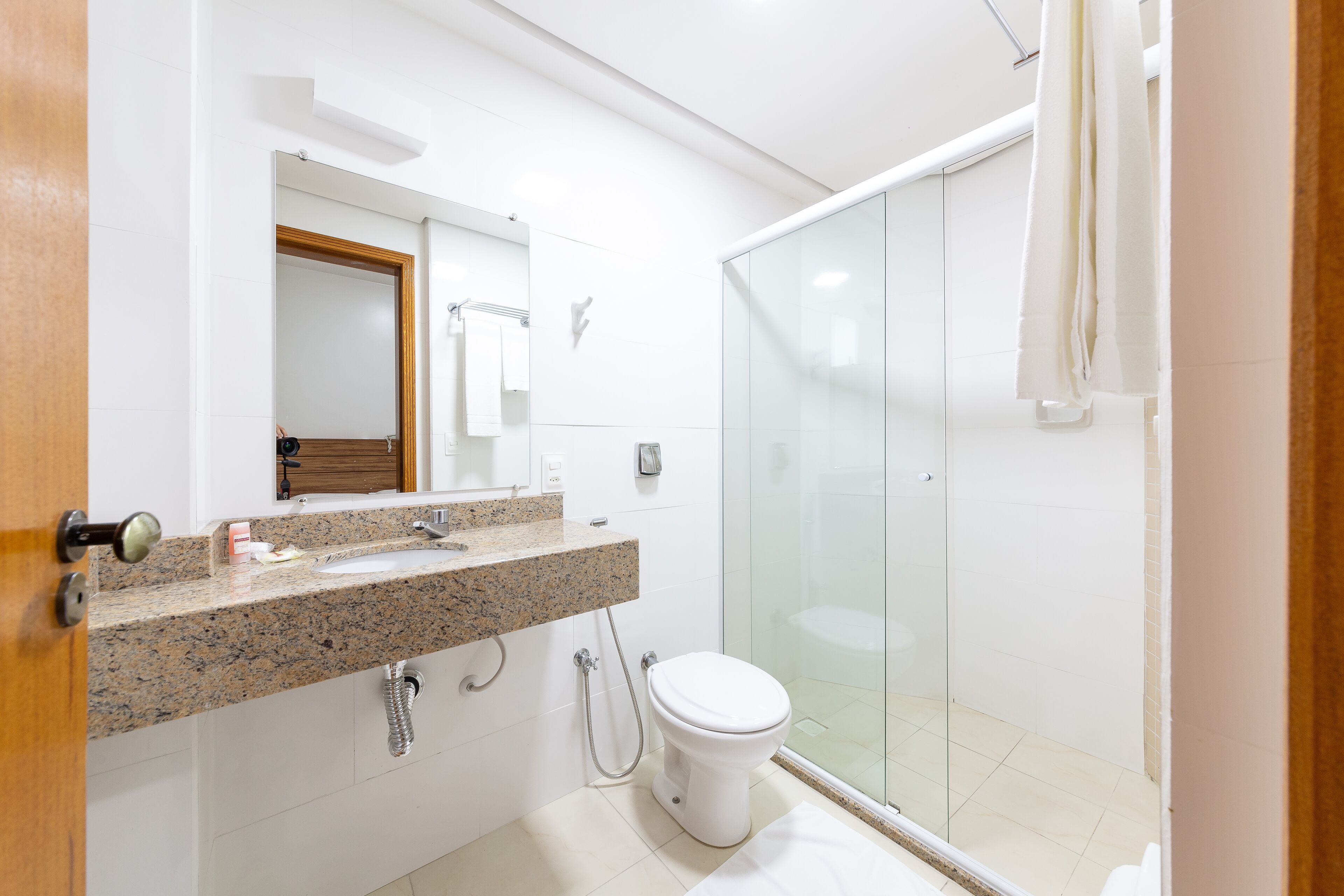 A modern bathroom with a granite countertop, a white toilet, and a glass shower enclosure.