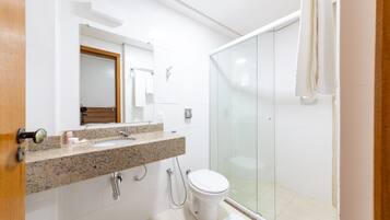 A modern bathroom with a granite countertop, a white toilet, and a glass shower enclosure.