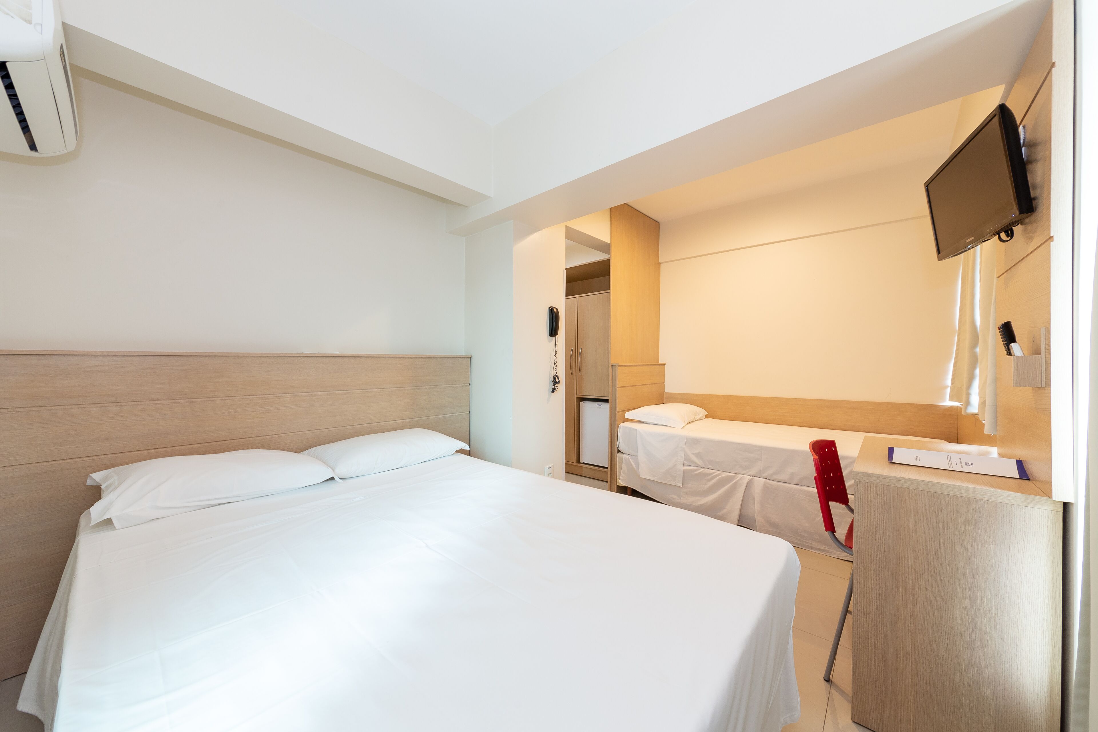 Quarto de hotel com duas camas, uma mesa, uma televisão e um telefone.