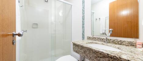 Un baño con cabina de ducha de vidrio, inodoro blanco y encimera de granito con lavamanos y espejo.