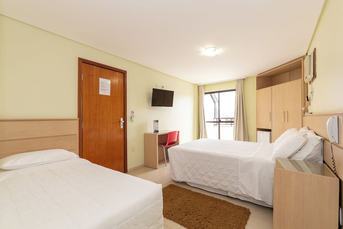 A hotel room with two beds, a desk, a TV, and a wardrobe.