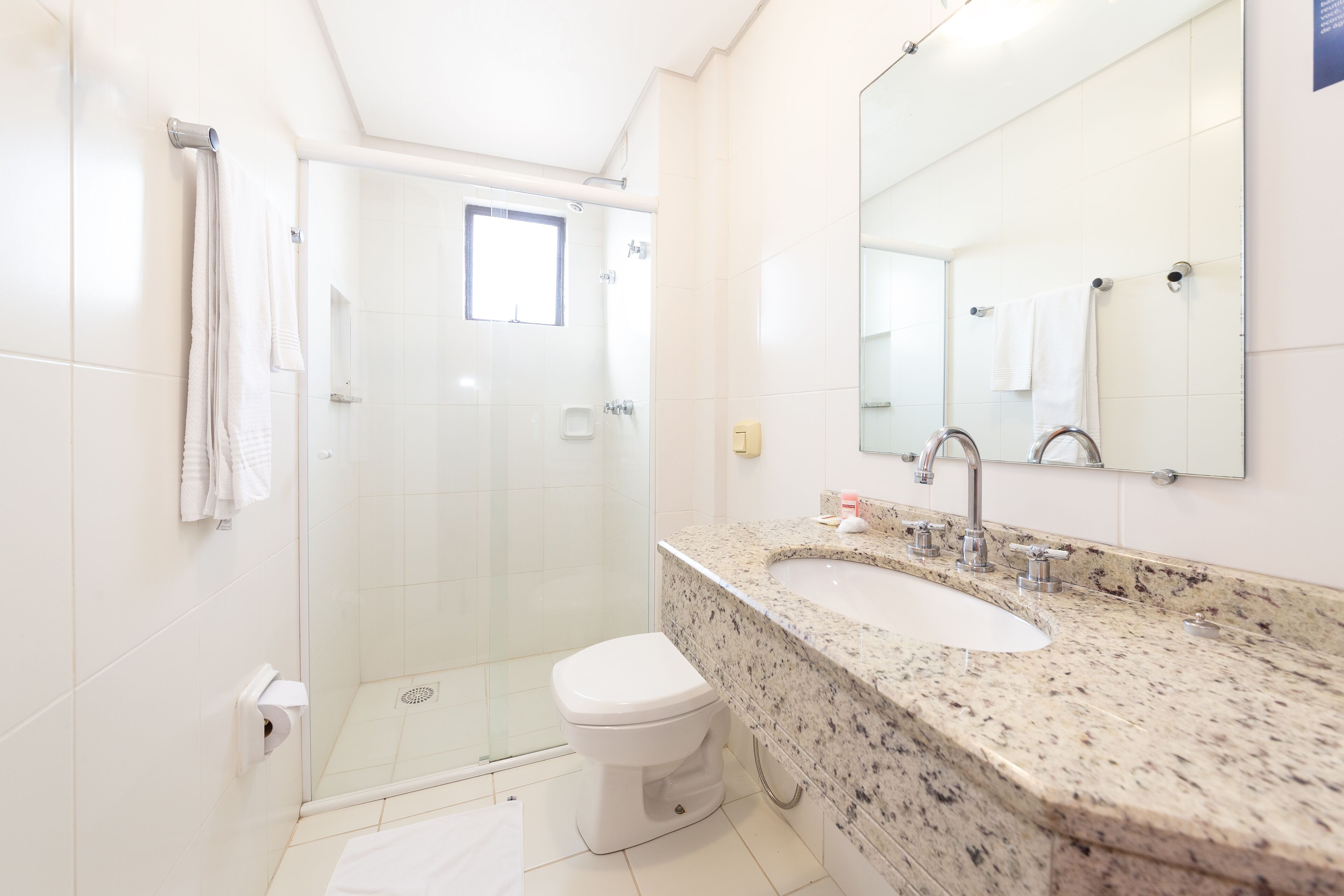 A modern bathroom with a glass-enclosed shower, a white toilet, and a granite countertop sink.