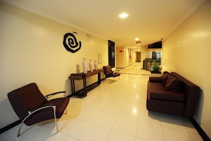 A hotel lobby with a reception desk, seating area, and a kitchenette in the background.