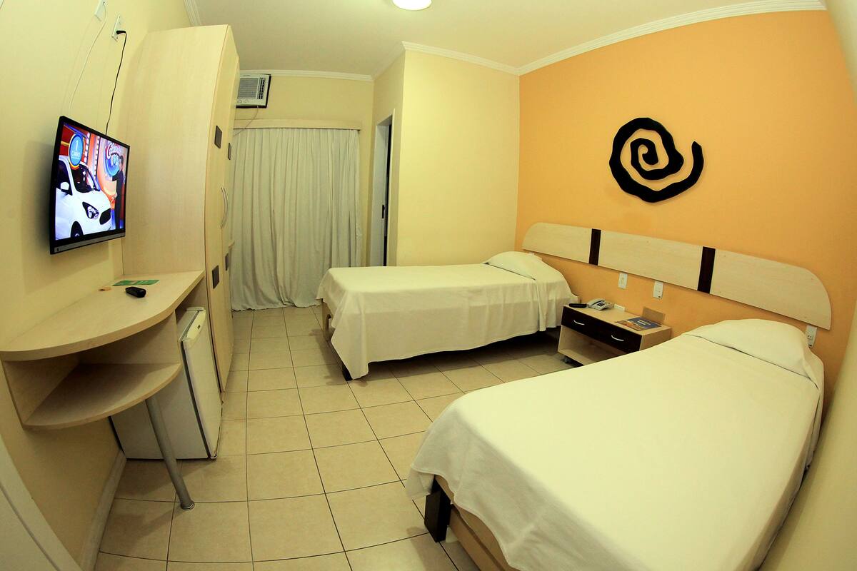 Habitación de hotel con dos camas, un escritorio, un televisor y una pared con un logotipo.