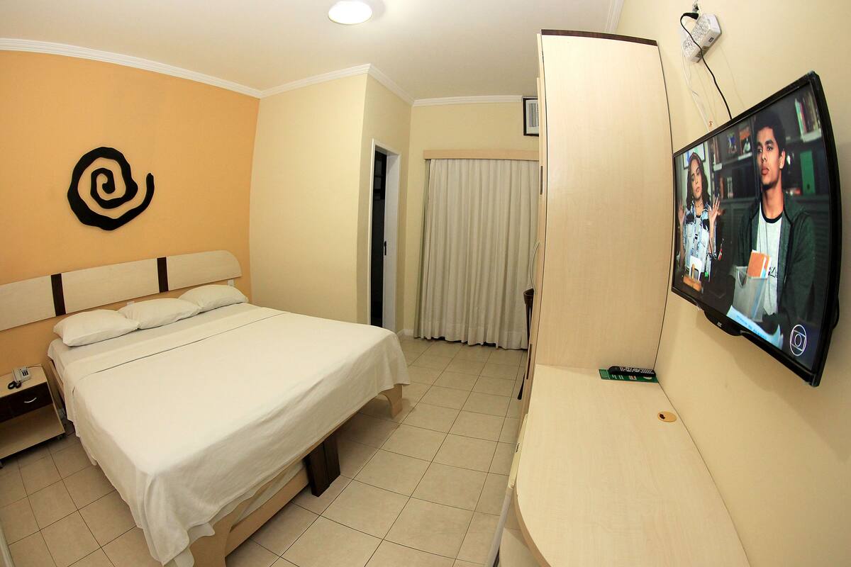 Una habitación de hotel con una cama, un televisor montado en la pared y una cortina.