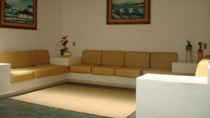 A living room with a beige sectional sofa, a white armchair, and two framed paintings on the walls. - Hotel Terra do Sol (Aracaju)