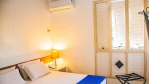 A hotel room with a bed, a nightstand with a lamp, an air conditioning unit, and a window with shutters. - Hotel Terra do Sol (Aracaju)