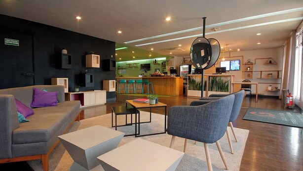 Eine moderne Hotelhalle mit einer Couch, Sesseln, einem Couchtisch und einem Empfangsbereich im Hintergrund.