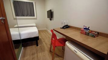 Ein kleines Hotelzimmer mit Bett, Schreibtisch, Stuhl, Fernseher und einem kleinen Kühlschrank.