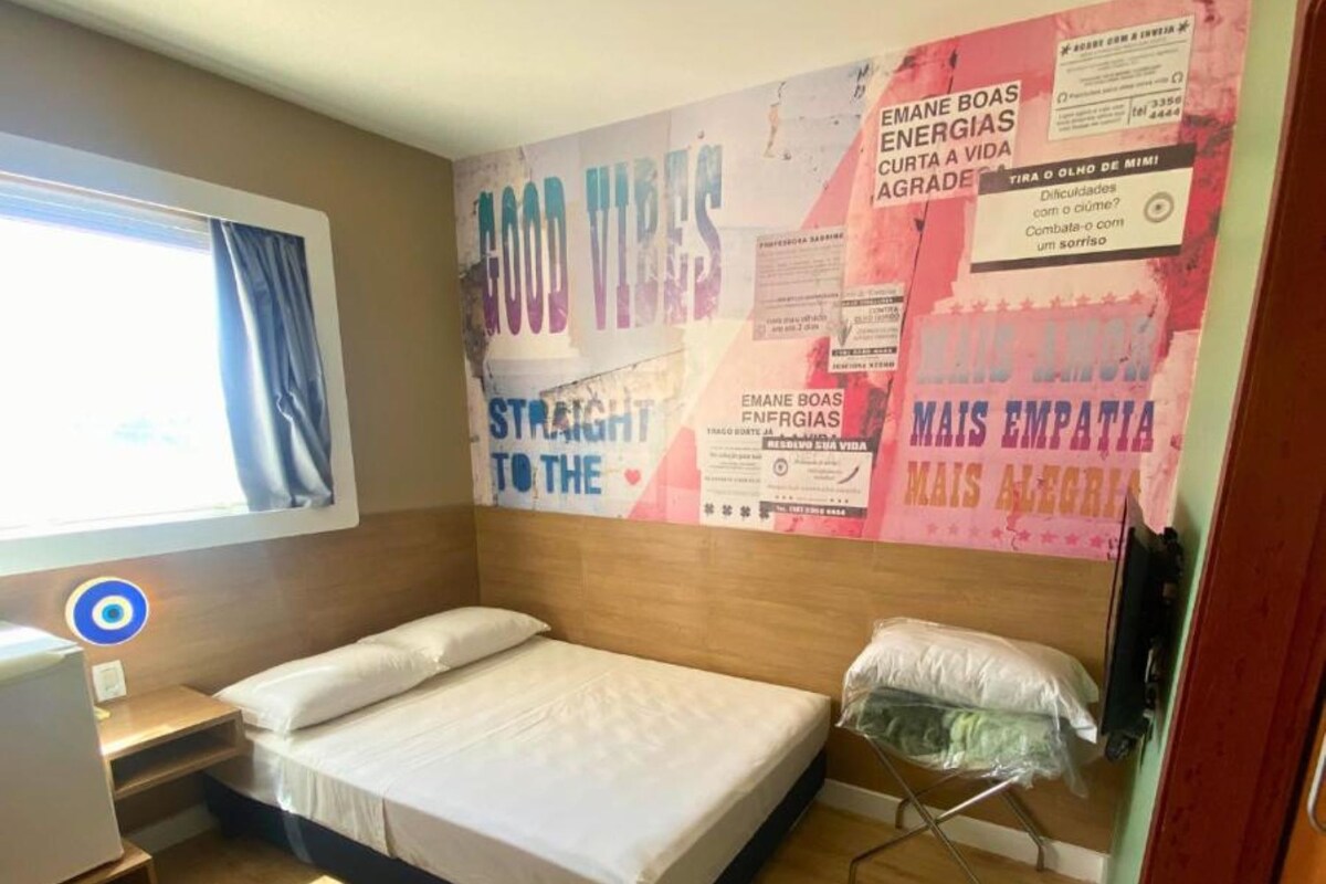 A small, neatly arranged room with a bed, a desk, and a window.