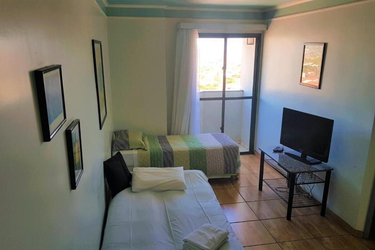 Una habitación con dos camas, un televisor sobre un mueble y una ventana con cortinas.