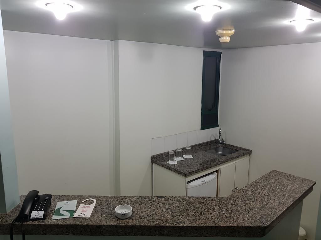 Uma cozinha pequena e compacta, com bancada de granito, pia embutida e armário branco. Há um telefone e um pequeno prato no balcão.