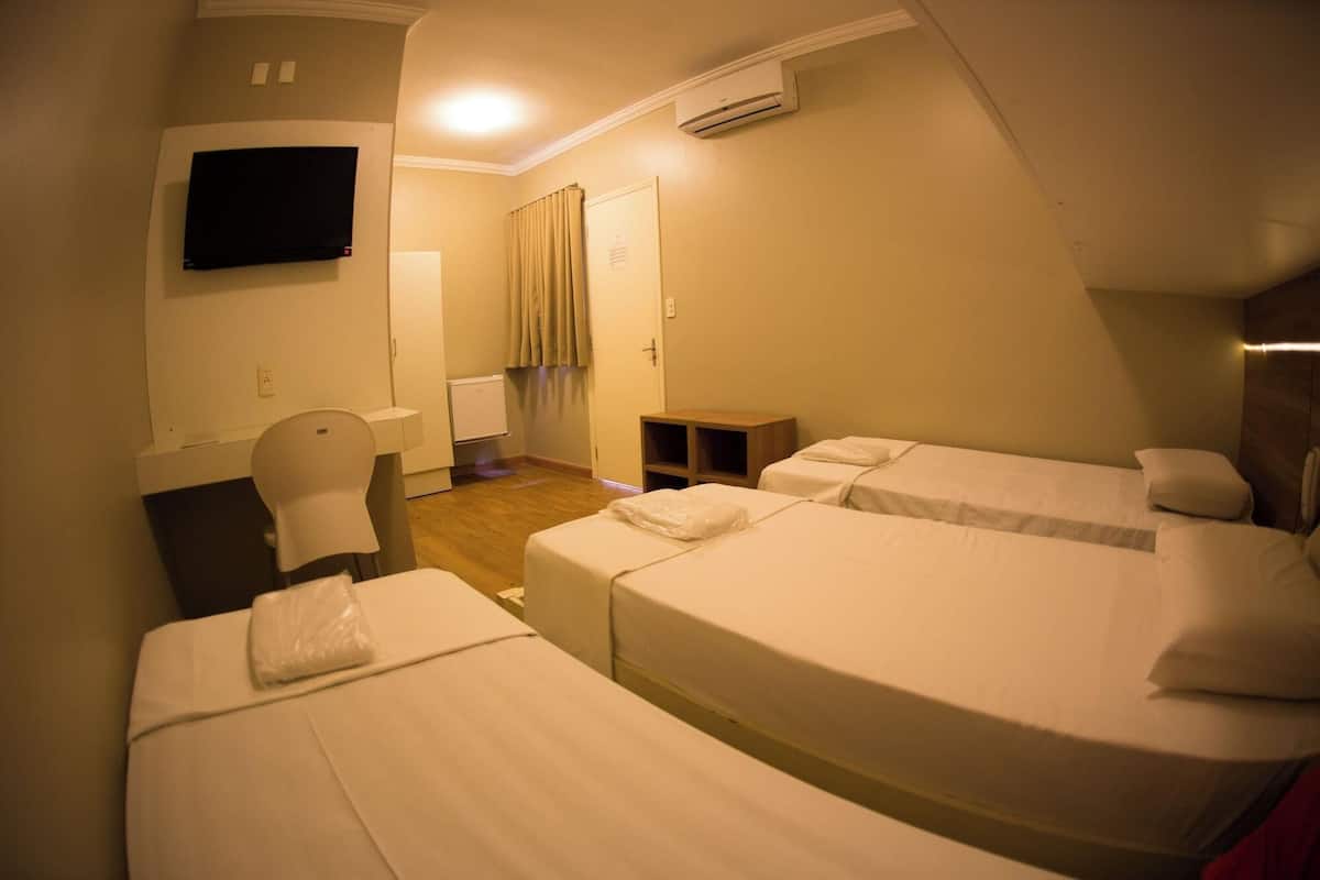 Ein Hotelzimmer mit zwei Betten, einem Fernseher, einem Schreibtisch, einem Stuhl, einem Kleiderschrank, einem kleinen Tisch und einer Klimaanlage.