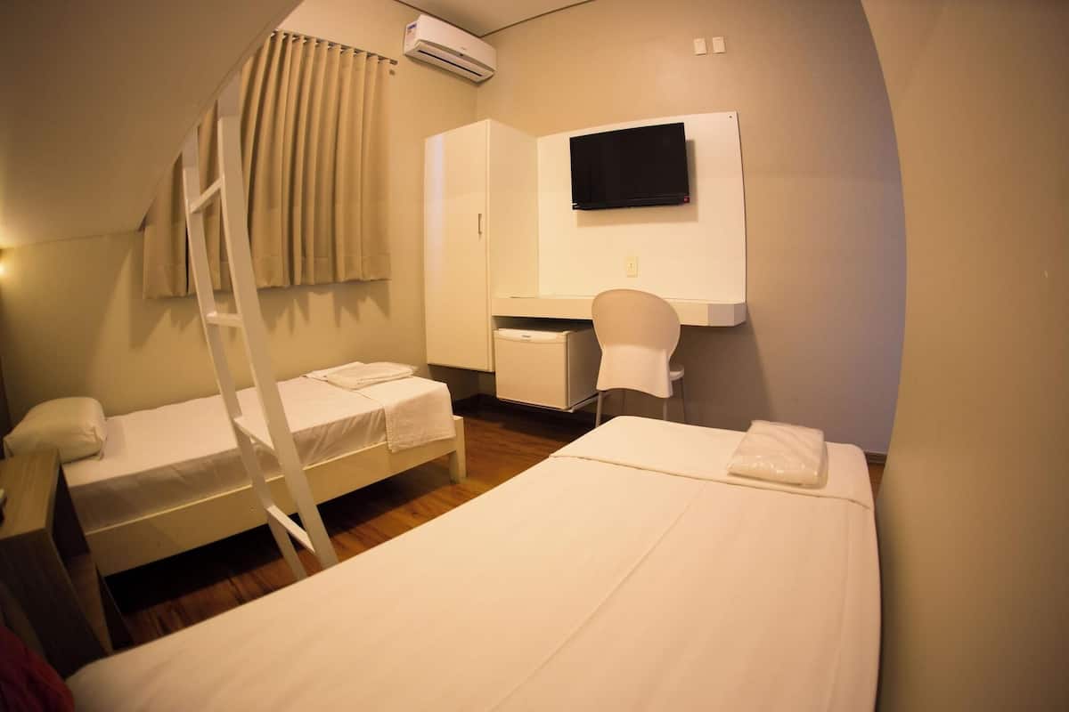 Ein Hotelzimmer mit zwei Einzelbetten, einem Schreibtisch mit Stuhl, einem flachbildfernseher an der Wand und einer Klimaanlage über der Tür.