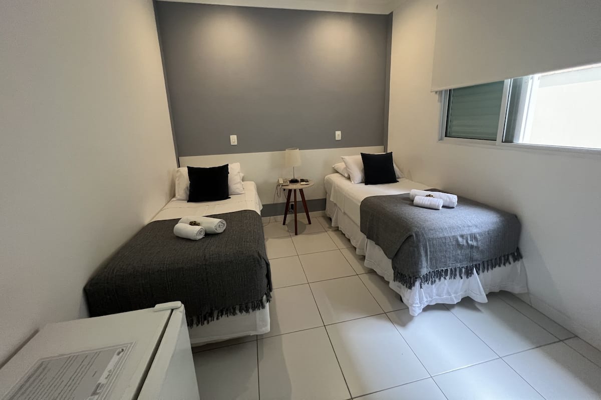 A small, clean room with two single beds, a small table, and a window.