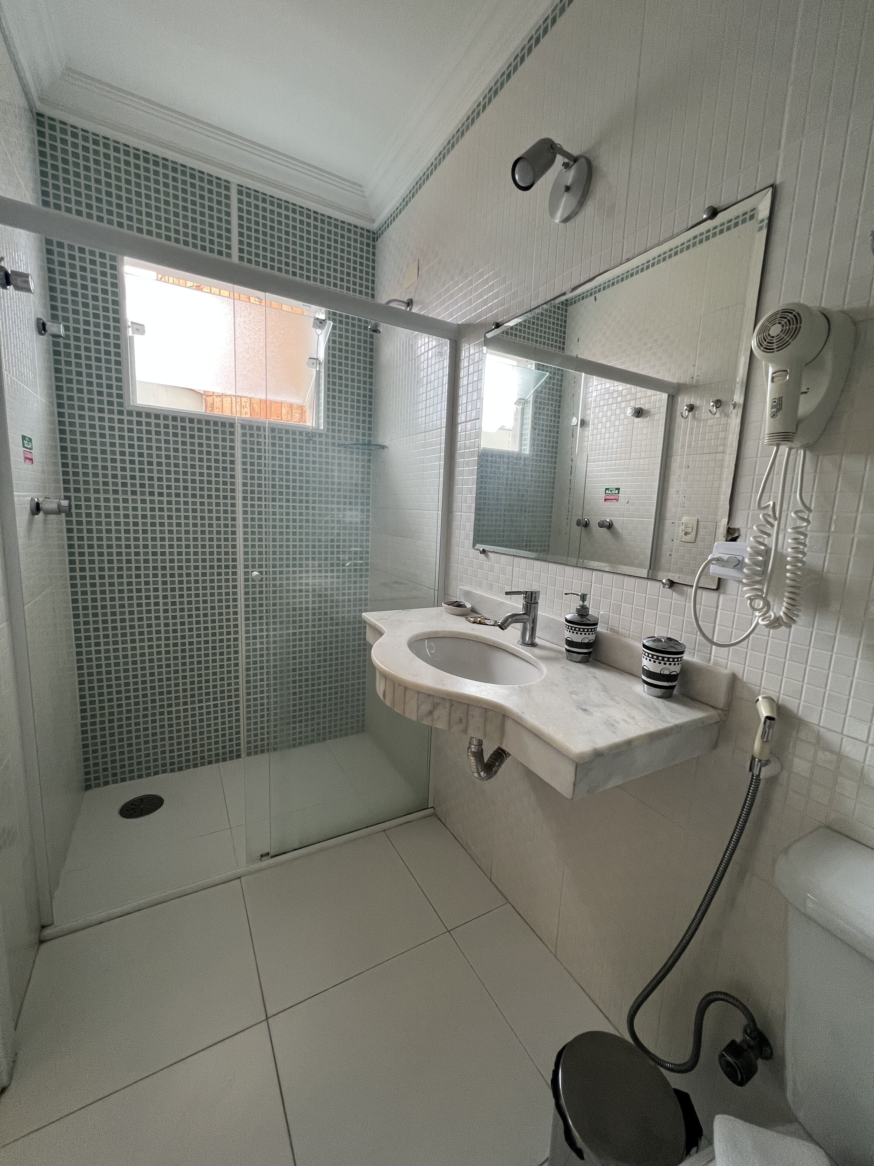 Un baño con cabina de ducha de vidrio, un lavamanos con espejo y un secador de pelo fijado en la pared.