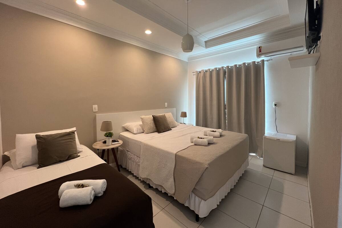 A hotel room with two beds, a small bedside table with a lamp, a TV mounted on the wall, and a shower area.