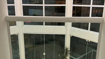 Een hoekperspectief van een hotelkamer met een groot erkerraam, een kamerplant en uitzicht op de ruimte beneden.