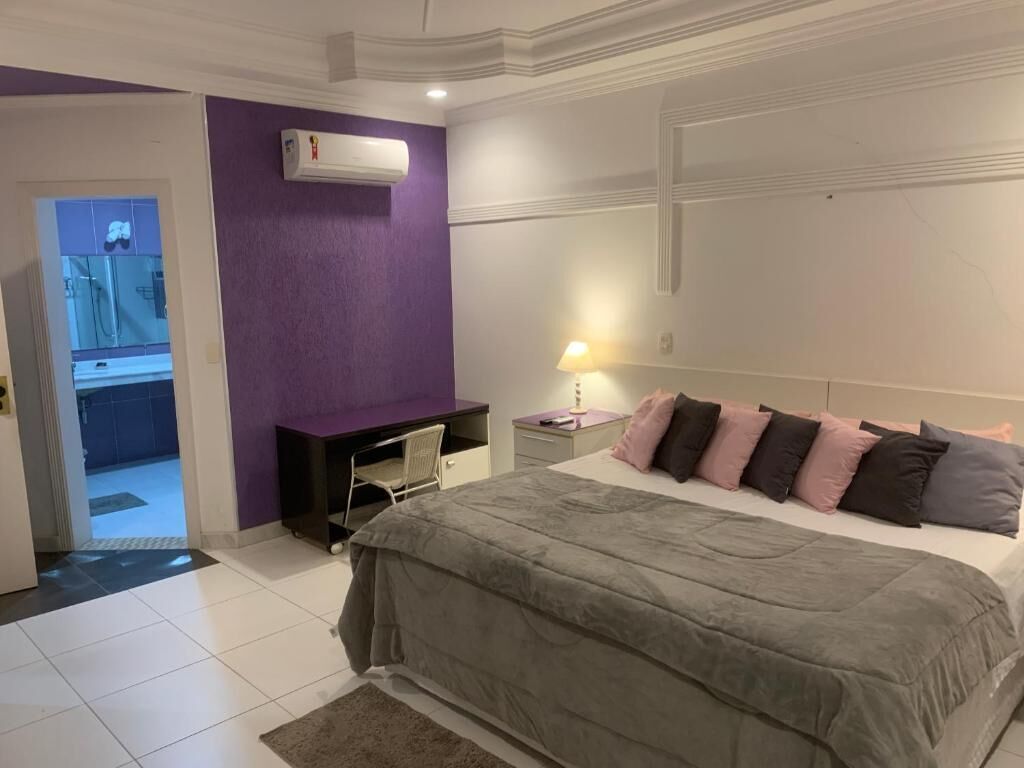 Ein Schlafzimmer mit einem Bett, einem Schreibtisch, einem Stuhl, einem Nachttisch, einer Lampe und einer Klimaanlage.