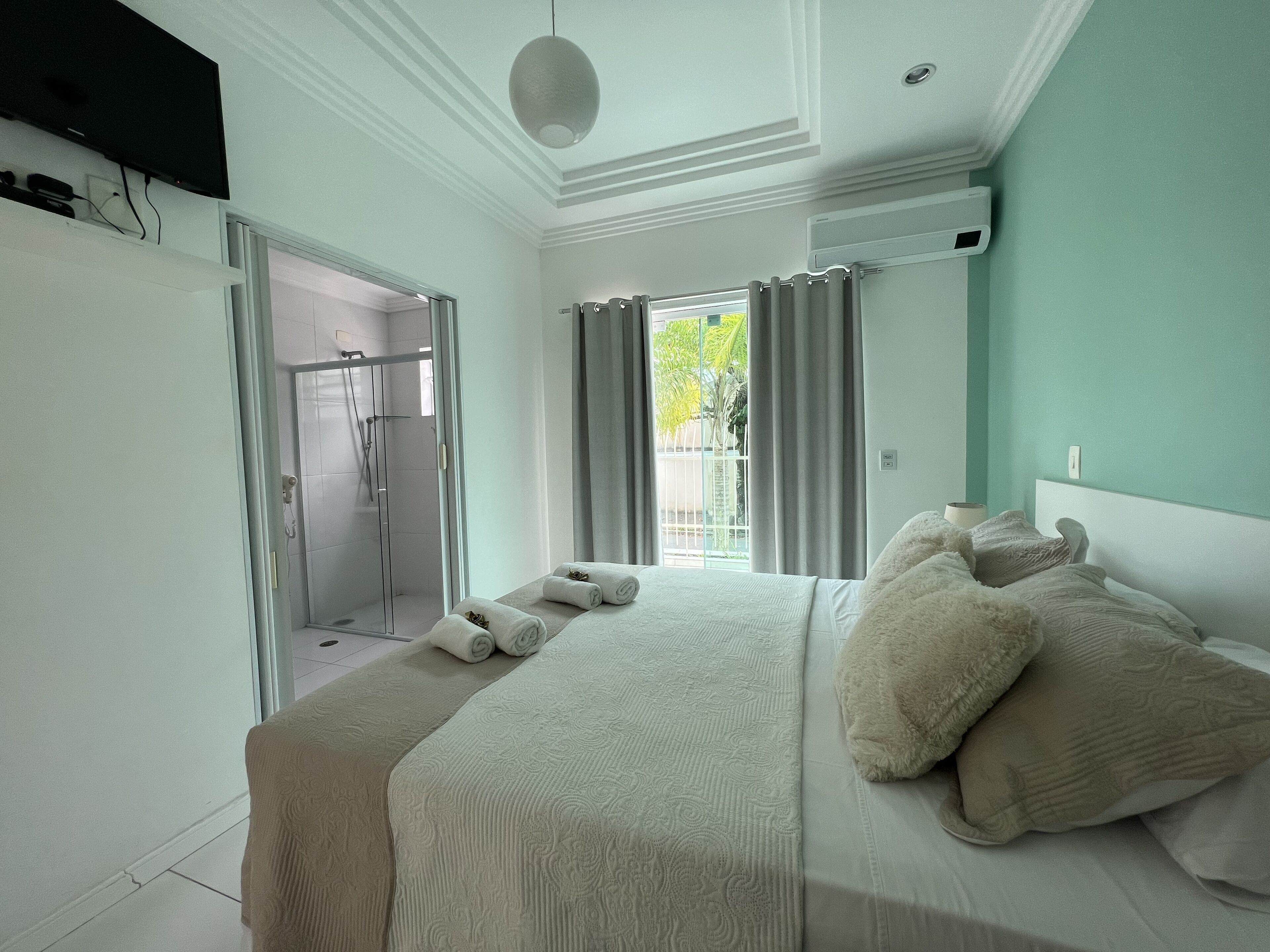 Ein modernes Schlafzimmer mit einem großen Bett, einer Dusche und Blick auf Grün.