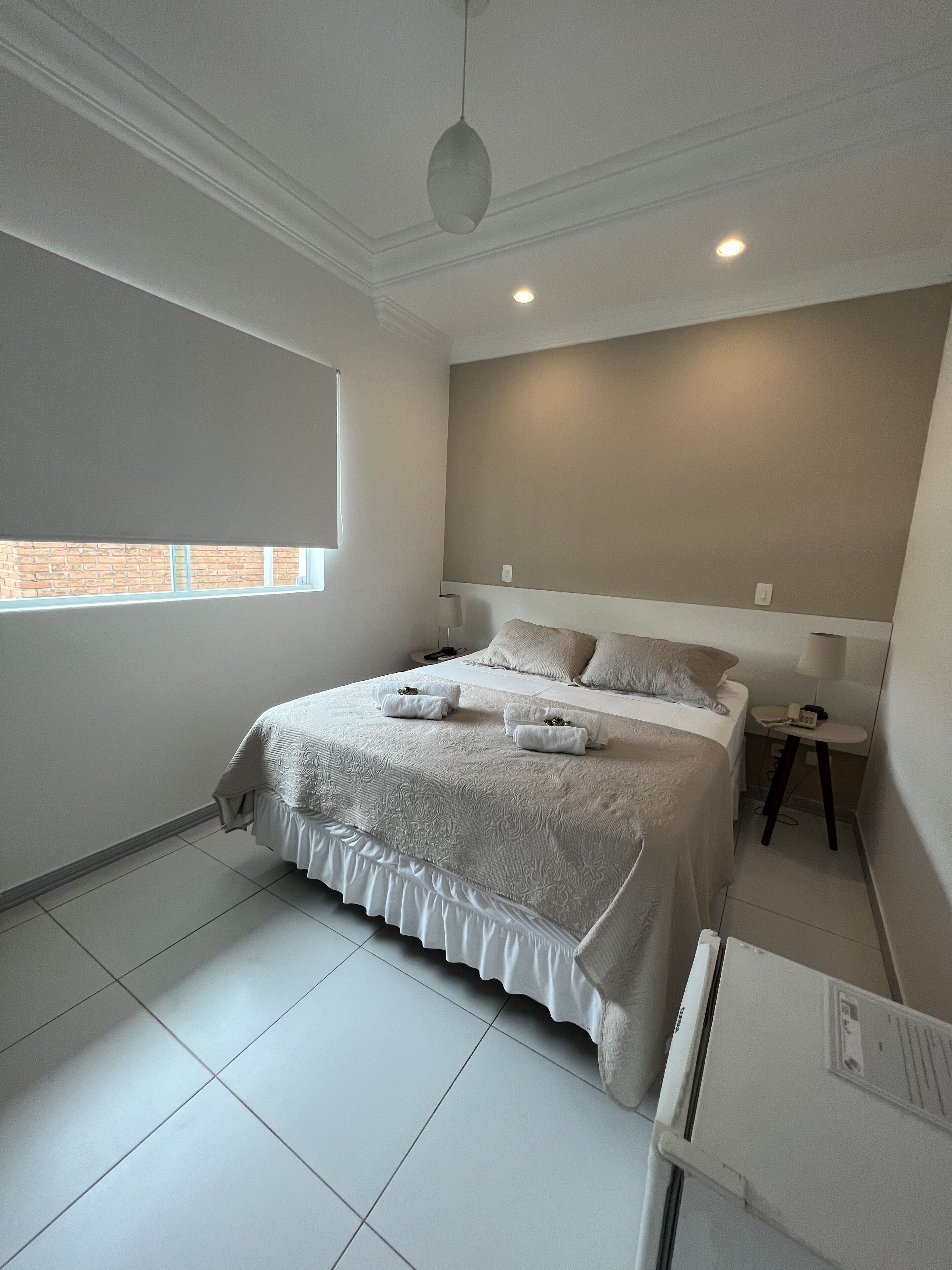 A bedroom with a large bed, a bedside table, a nightstand, and a window with a view of the outside.