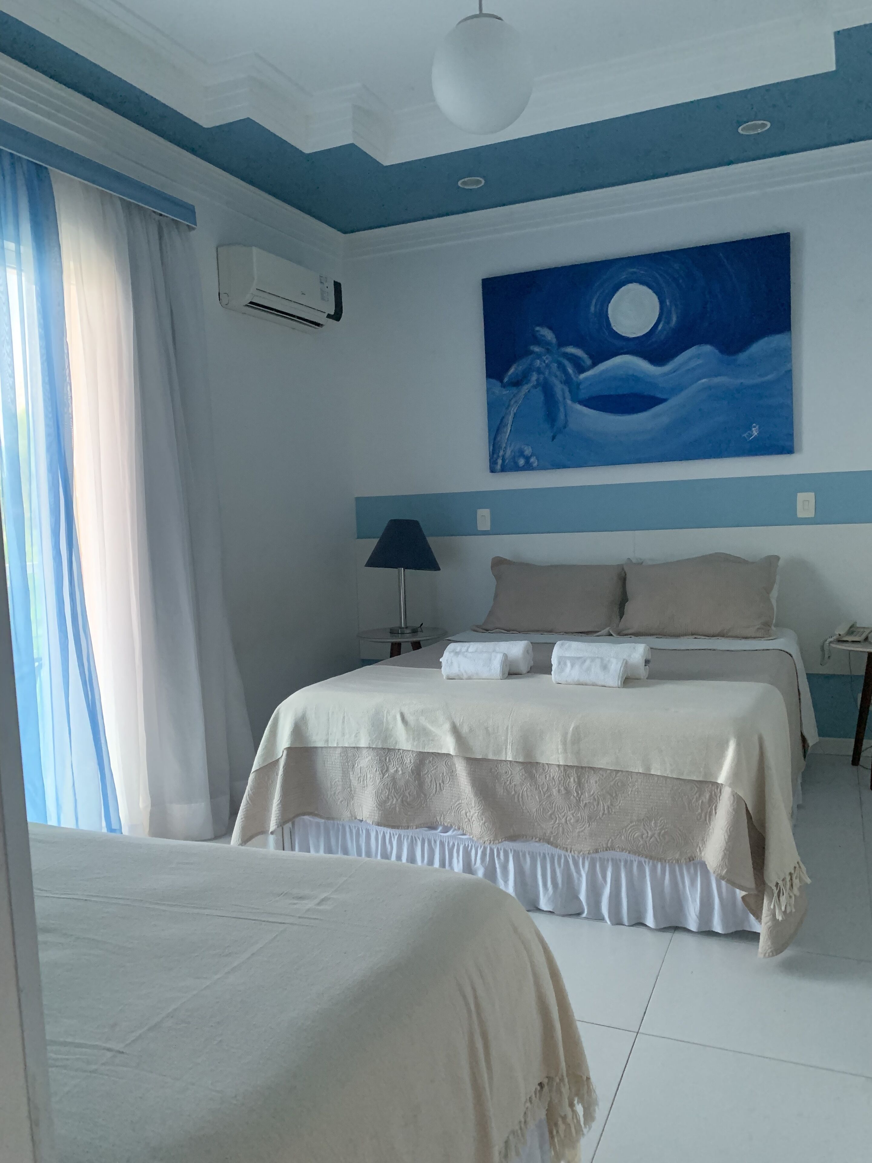 Habitación de hotel con dos camas, un cuadro de una playa a la luz de la luna, un ventilador de techo y una ventana con cortinas.