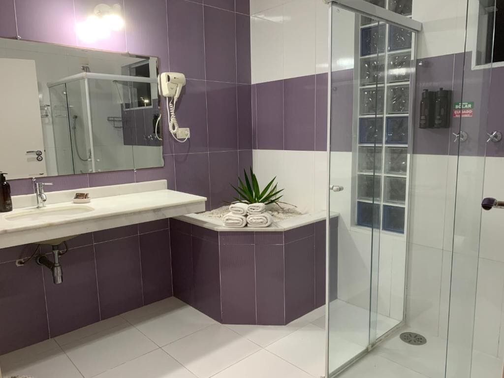 A modern bathroom with a glass shower enclosure, a sink with a mirror, and a small plant on a pedestal.