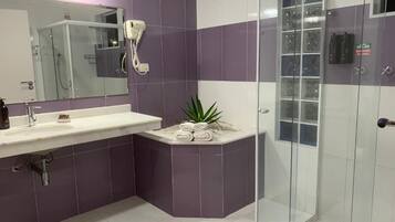 A modern bathroom with a glass shower enclosure, a sink with a mirror, and a small plant on a pedestal.