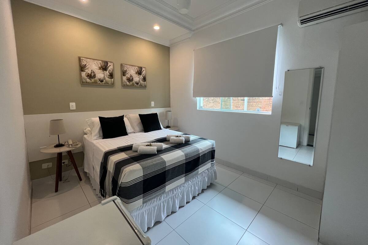 A hotel room with a bed, bedside table, lamp, and artwork on the wall.