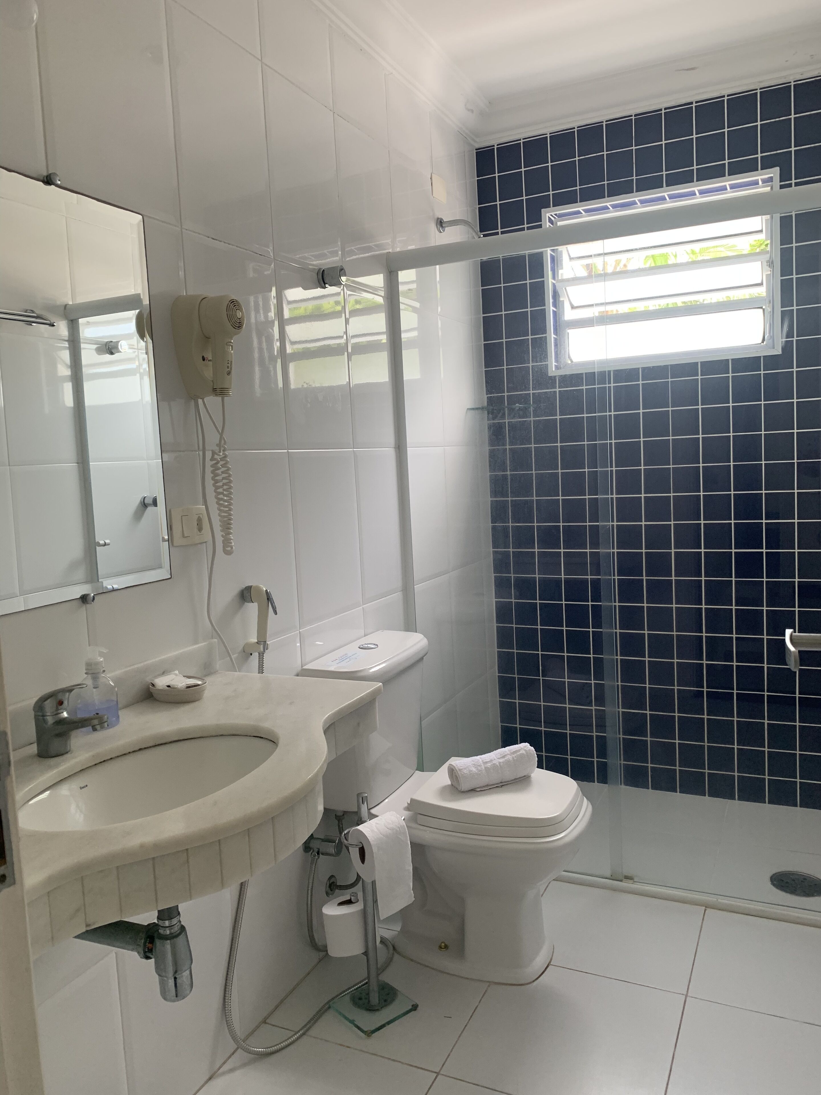 Casa de banho com lavatório branco, sanita e chuveiro, e espelho.