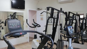 Un gimnasio con diversas máquinas de ejercicio, un televisor en la pared y un equipo de aire acondicionado.