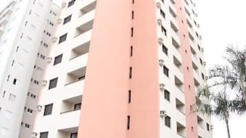A high-rise building with a pink and white facade, featuring multiple balconies and air conditioning units.