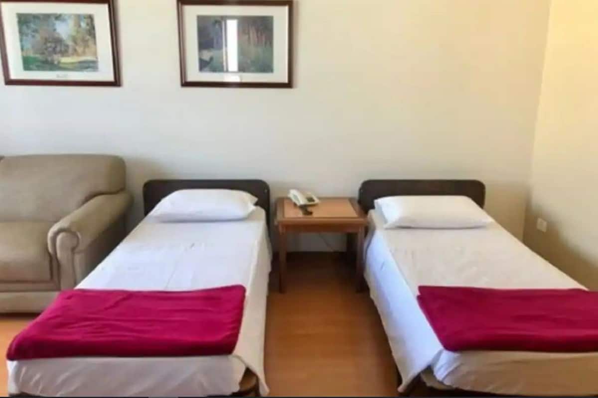 A hotel room with two single beds, a sofa, a bedside table with a phone, and framed pictures on the wall.