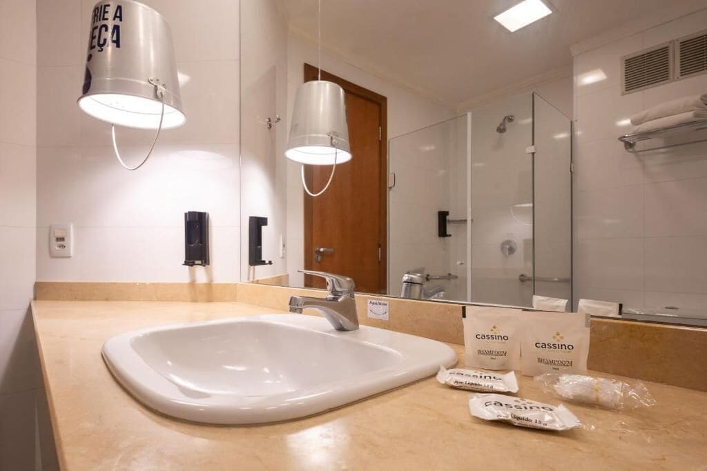 Une salle de bain moderne avec un grand lavabo, deux lampes suspendues, un miroir et des articles de toilette posés sur le comptoir.