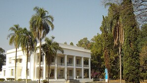 Un edificio blanco con un porche central y columnas, rodeado de palmeras y un cielo despejado.