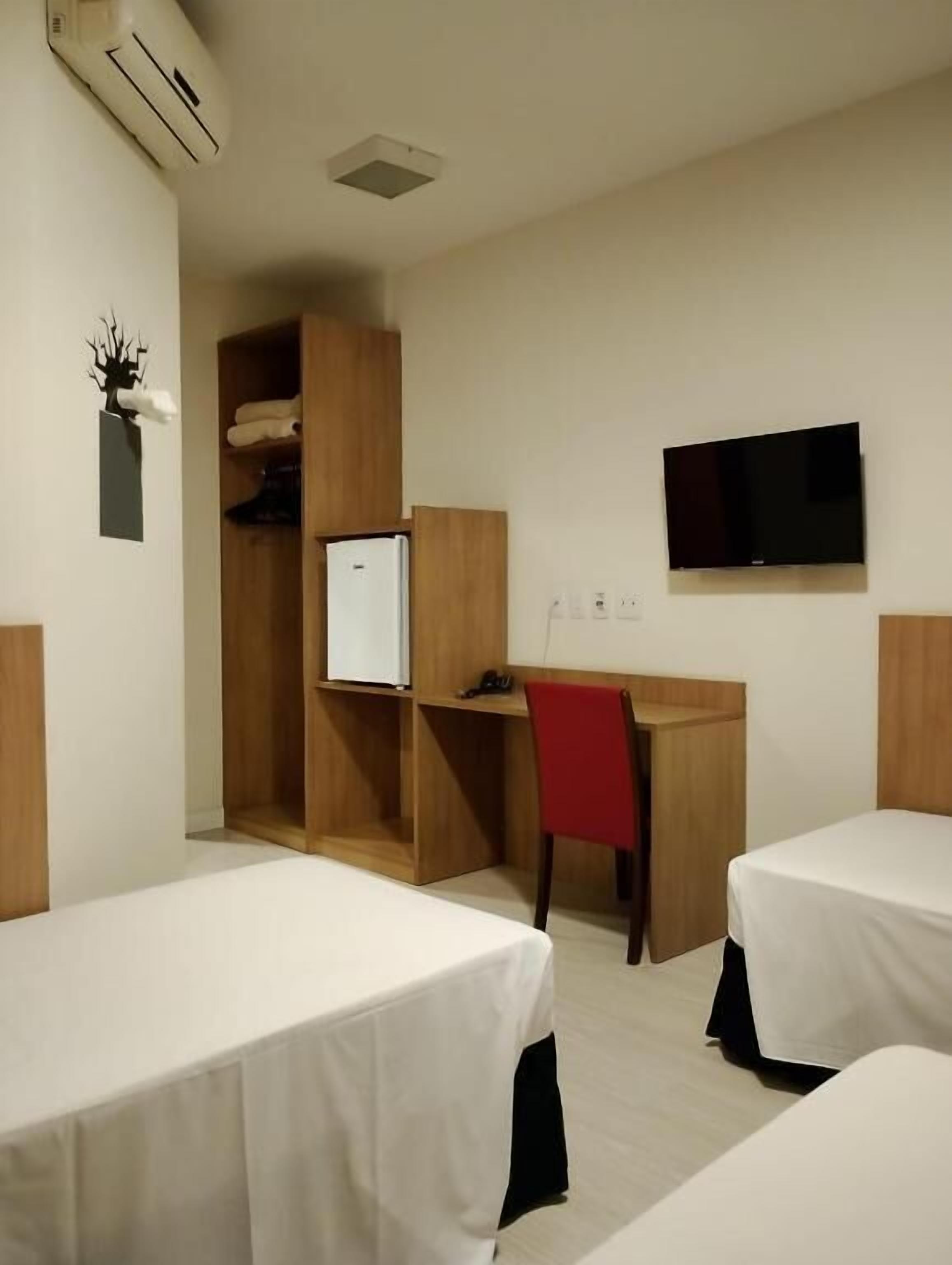 A hotel room with two beds, a desk with a chair, a television, and a wardrobe.