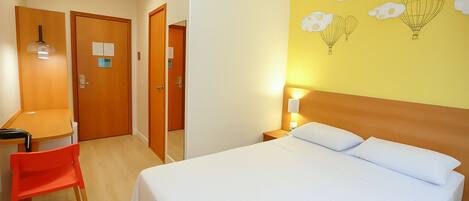 A hotel room with a bed, a desk, a chair, and a wall with hot air balloon artwork.