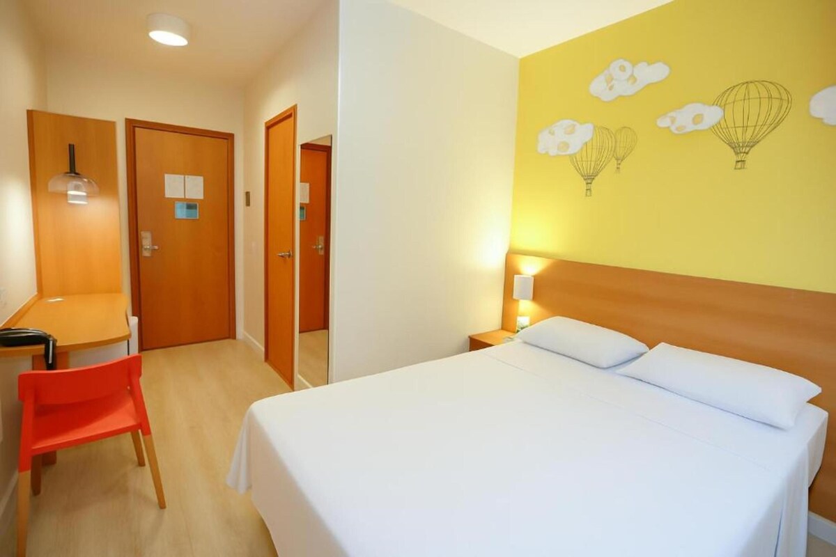 A hotel room with a bed, a desk, a chair, and a wall with a hot air balloon design.