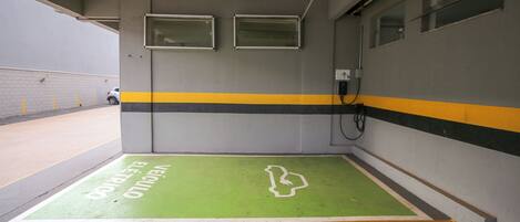 Un garaje para estacionar con zonas pintadas de verde y amarillo, un espacio accesible para sillas de ruedas y un cuadro eléctrico fijado a la pared.