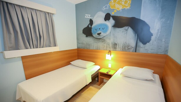 A hotel room with two single beds, a wooden headboard, a nightstand with a lamp, and a wall mural of a panda.