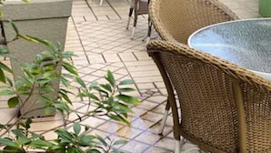 A patio area with wicker chairs and a table, surrounded by potted plants and a green wall.