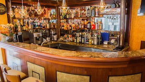 A bar area with a curved counter, multiple shelves of liquor bottles, a coffee machine, and three bar stools.